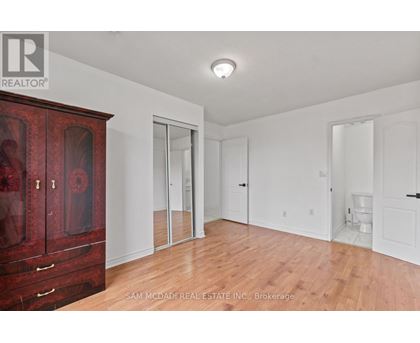 A room with a wooden floor and white walls, with a red cabinet on the left and a toilet in the distance.