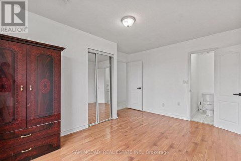 A room with a wooden floor and white walls, with a red cabinet on the left and a toilet in the distance.