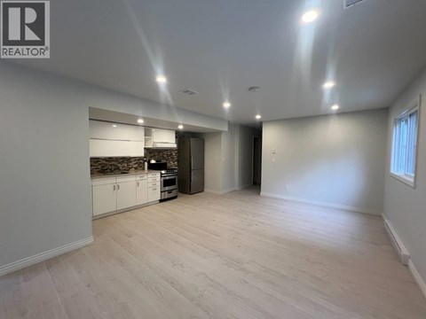 A spacious room with a kitchen area and a door leading to another room.