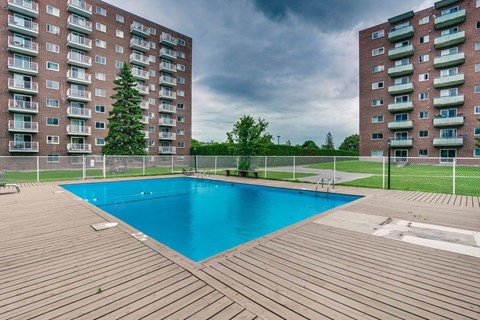 A pool in a backyard surrounded by two apartment buildings.