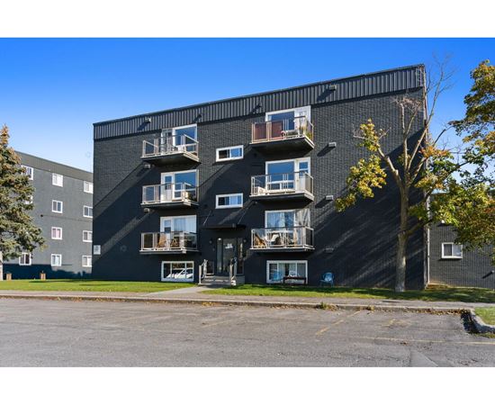 A black apartment building with balconies and trees in the background.