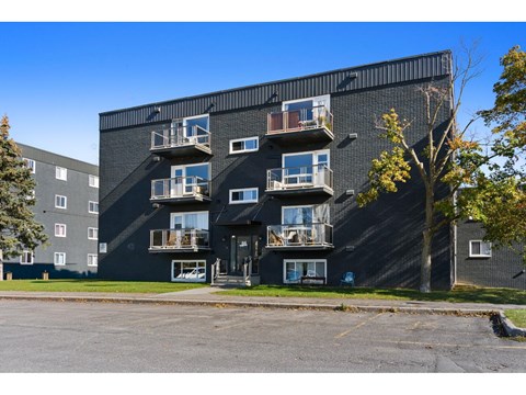 A black apartment building with balconies and trees in the background.