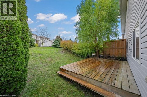 A wooden deck leads to a house with a well-kept lawn and trees.