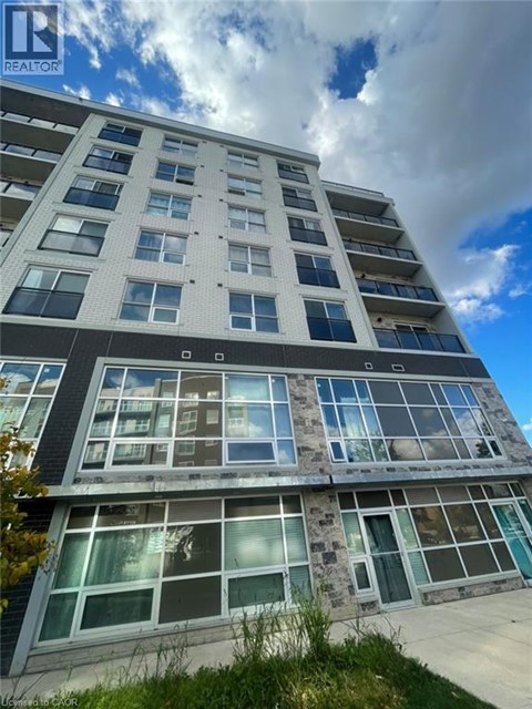 A tall building with many windows and balconies is shown under a blue sky.