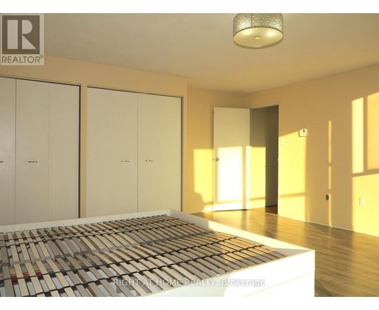 A bedroom with a bed in the foreground and a realtor logo on the wall.