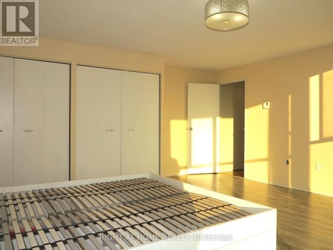A bedroom with a bed in the foreground and a realtor logo on the wall.
