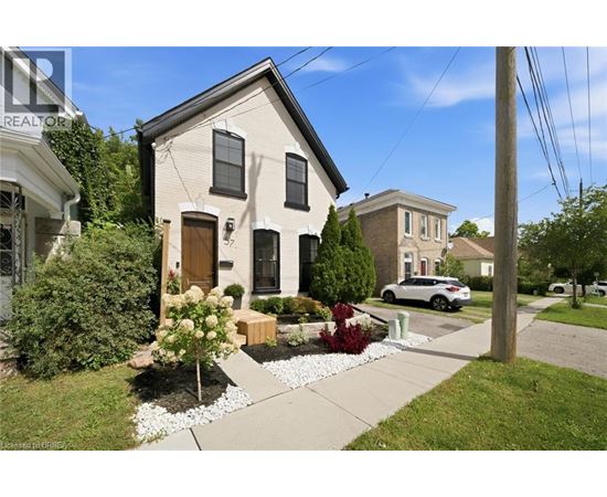 A house with a brown door and windows is surrounded by a garden and a sidewalk.