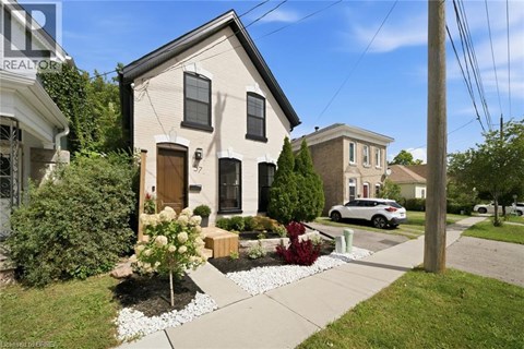 A house with a brown door and windows is surrounded by a garden and a sidewalk.