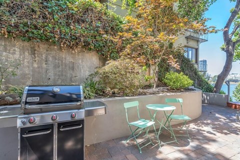 A BBQ grill is on a patio with a table and chairs.