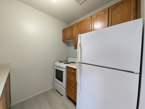 A white refrigerator stands in a kitchen with wooden cabinets and a stove.