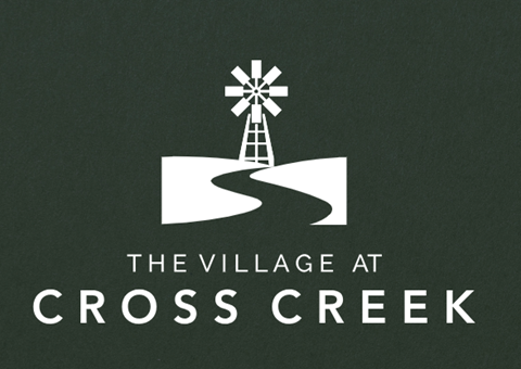 A logo with a windmill on a green background that says "The Village at Cross Creek".