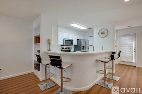 A kitchen with white walls and wooden floors has a bar area with two stools.