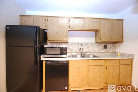 A kitchen with a black refrigerator, wooden cabinets, and a granite countertop.