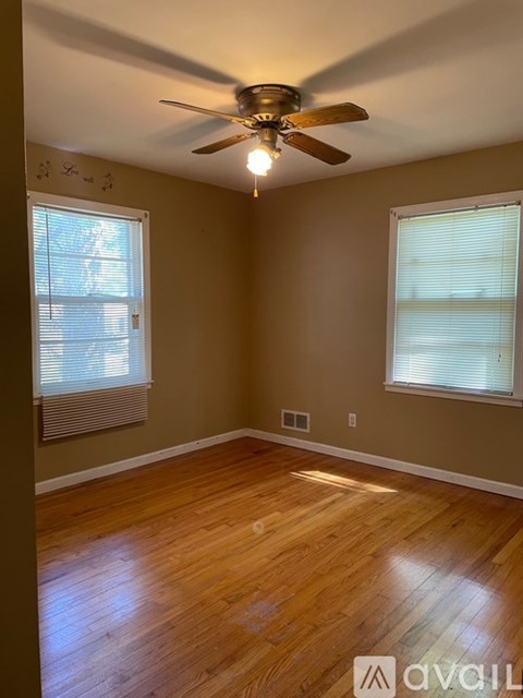 A room with a ceiling fan and two windows.