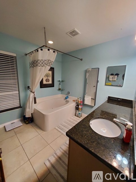 A bathroom with a white tub, sink, and a window with blinds.