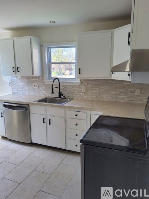 A kitchen with white cabinets and a black trash bin.