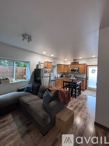A living room with a grey couch and a kitchen area with wooden cabinets.