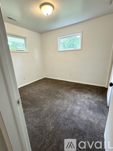 A room with a carpeted floor and two windows.