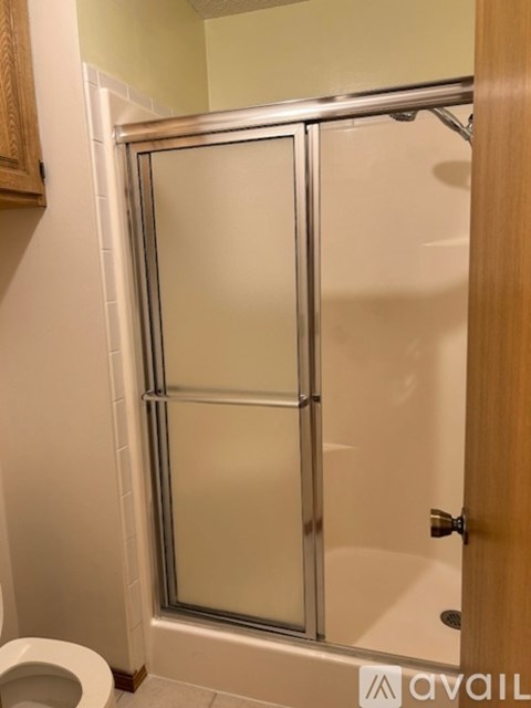 A bathroom with a toilet, a shower with a glass door and a wooden cabinet.