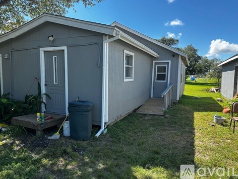 A grey house with a white door and windows is surrounded by a grassy area.