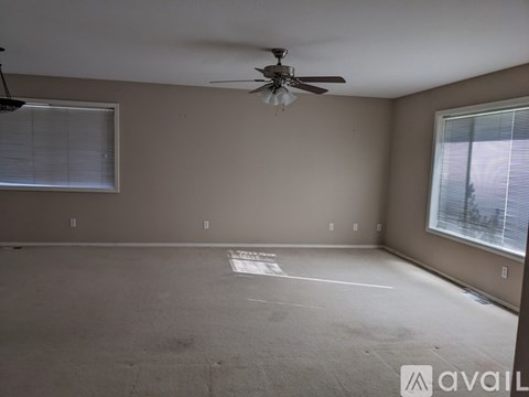 A spacious room with a ceiling fan and two windows.
