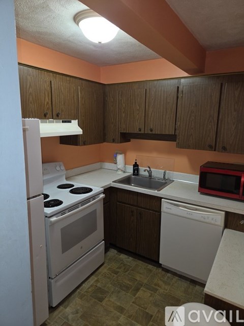 A kitchen with a white refrigerator, a white dishwasher, a red microwave, and brown cabinets.