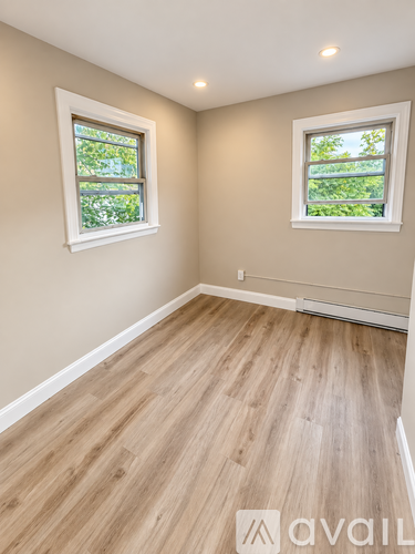 A room with wooden flooring and two windows.