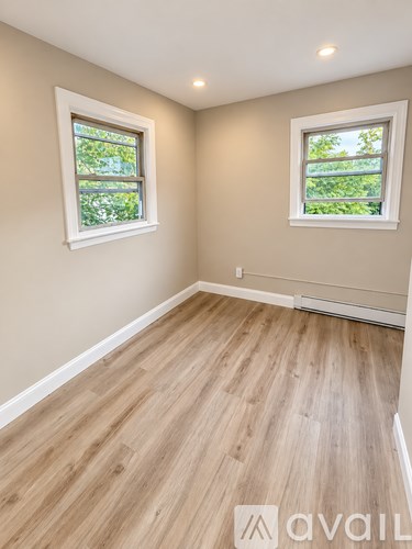 A room with wooden flooring and two windows.