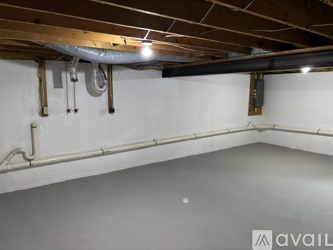 A room with a white wall and a ceiling with wooden beams and pipes.