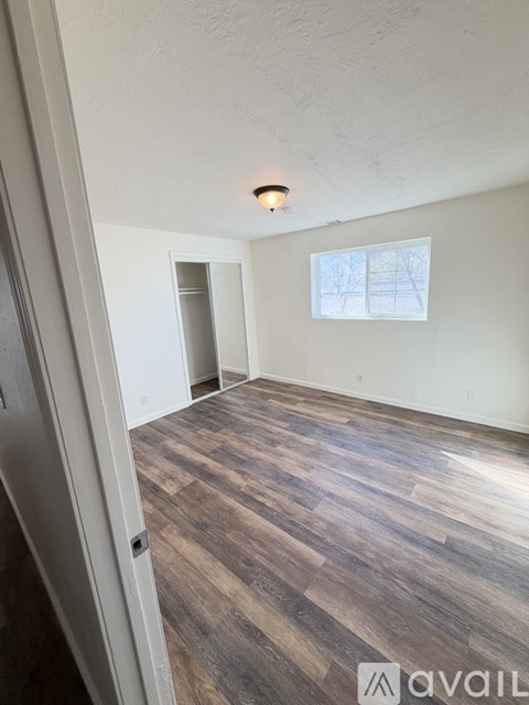A room with wooden flooring and a window showing trees outside.