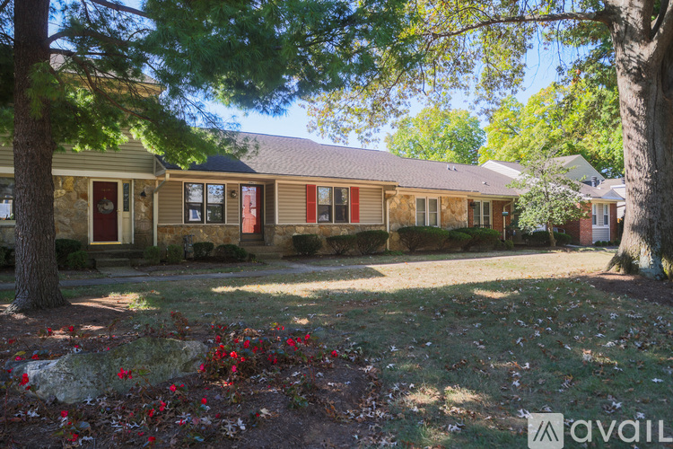 A house with a red door is surrounded by trees and has a grassy front yard.