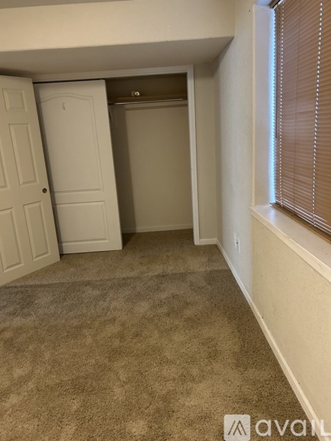 A carpeted room with a door and a window with blinds.