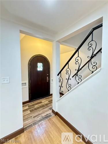 A hallway with a wooden door and a staircase with a black railing.