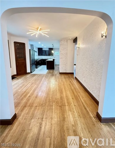 A hallway with wooden floors and a kitchen area in the background.