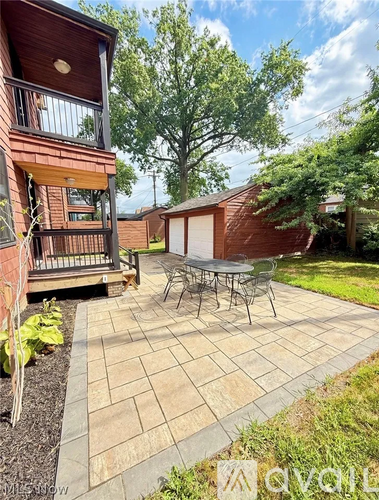 A patio with a table and chairs is surrounded by a brick building and trees.