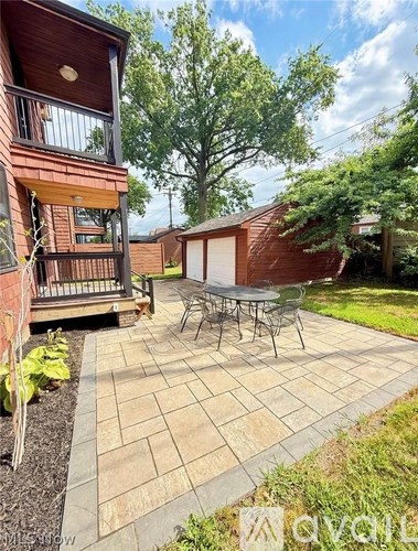 A patio with a table and chairs is surrounded by a brick building and trees.
