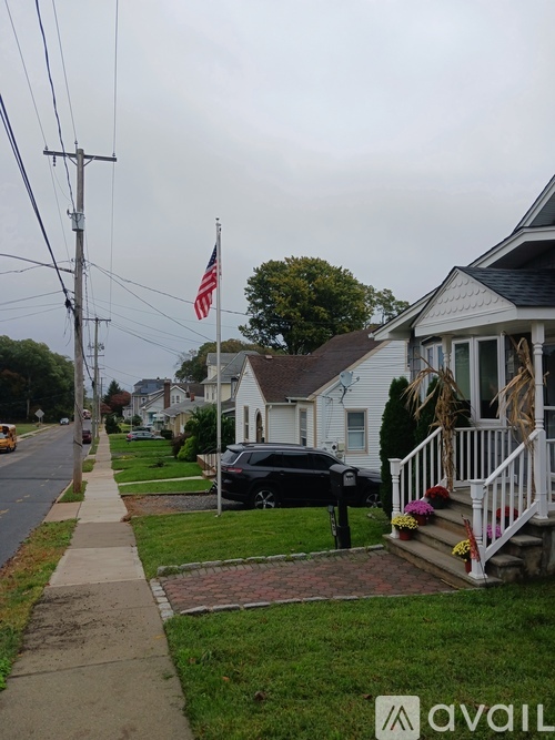 A black car is parked in front of a house with a flag on the telephone pole.
