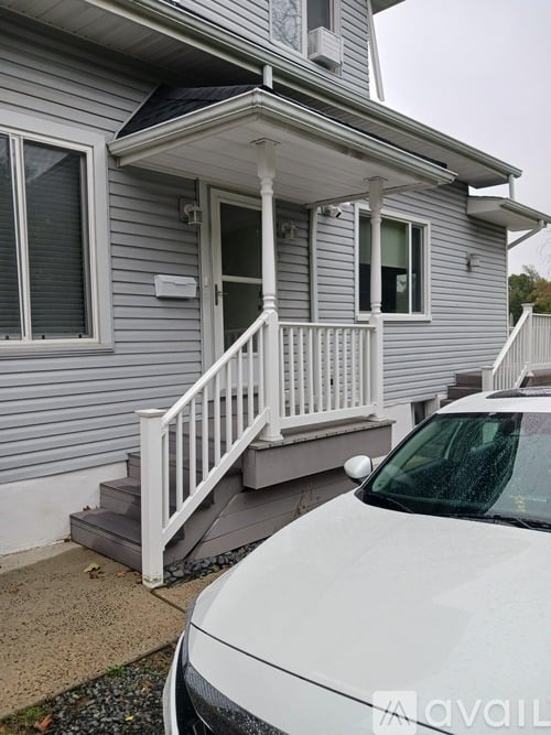 A white car is parked in front of a grey house.