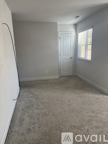 A room with a carpeted floor, a white door, and a window with blinds.