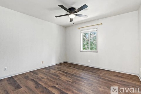 A room with a ceiling fan and a window with a view of trees.