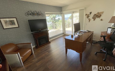 A living room with a brown leather couch, a wooden desk, and a television.