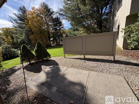 A backyard with a fence, trees, and a sidewalk.