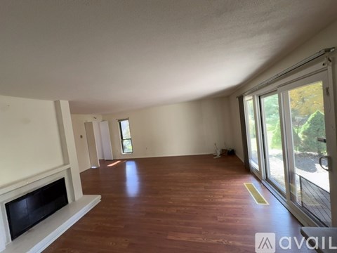 A spacious room with wooden flooring and a fireplace on the left side.