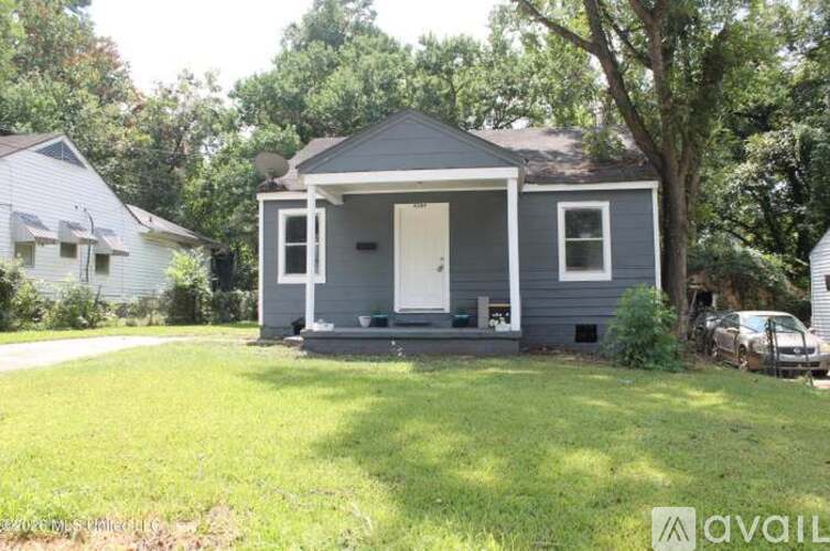 A gray house with a white door and windows is surrounded by greenery.
