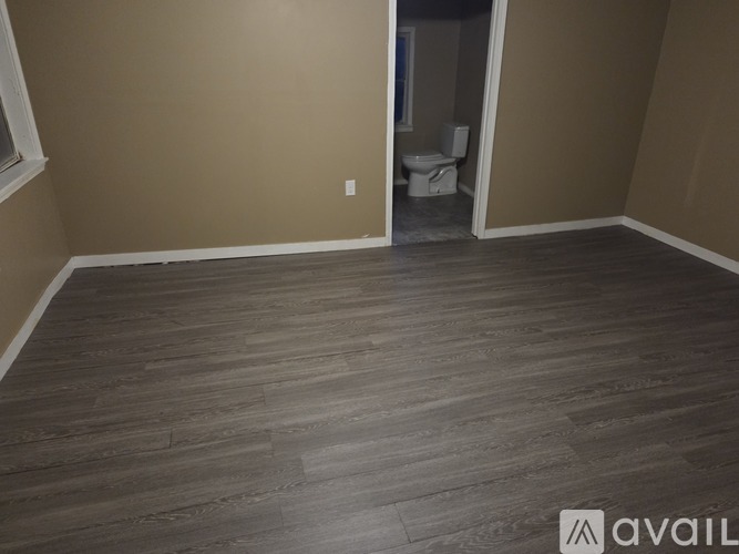 A room with wooden flooring and a toilet in the background.