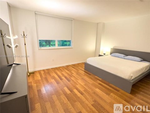 A bedroom with a bed, a dresser, and a window with blinds.