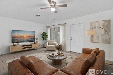 A living room with a brown leather sofa, a wooden coffee table, a flat screen TV, a ceiling fan, and a painting on the wall.