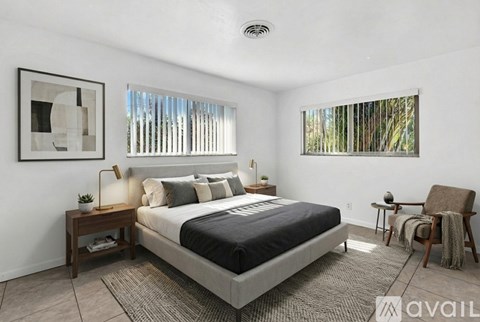 A bedroom with a large bed, a chair, and a window with blinds.