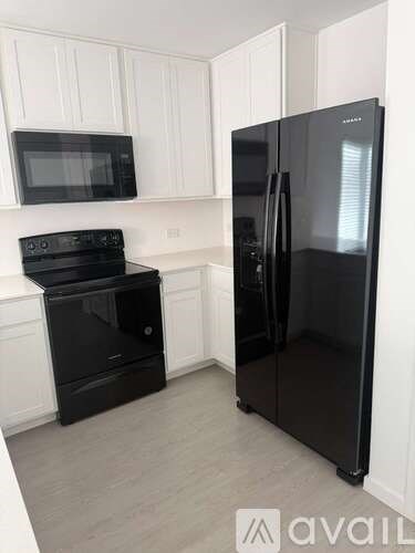 A black fridge and oven in a kitchen with white cabinets.