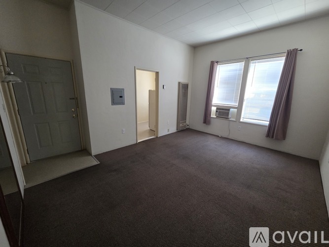 A room with a carpeted floor, a window with curtains, and a door.